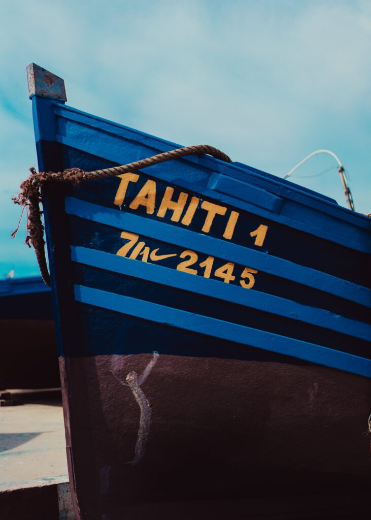 Blå fiskebåd med navnet "Navngivning af båd tahiti 1" med registreringsnummer "71c 2145" på en strand under klar himmel.